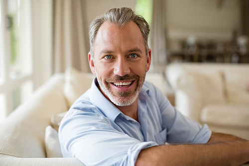 Portrait of smiling man sitting on sofa in living room at home