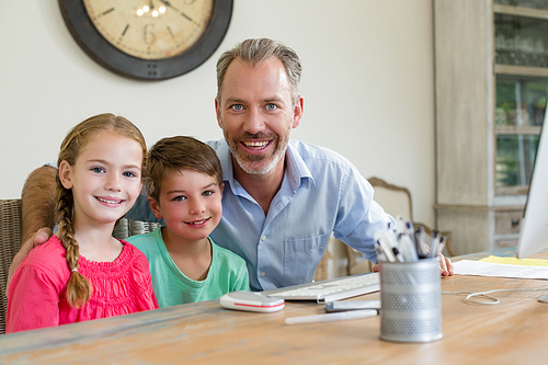 Portrait of happy father and kids sitting at desk