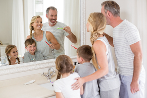 Smiling parents and kids brushing teeth in bathroom at home