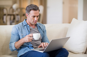 Man using laptop while having coffee in living room at home