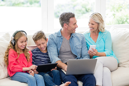Parents and kids using digital tablet, mobile phones and laptop in living room