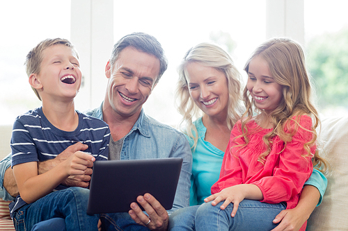 Smiling parents and kids using digital tablet in living room