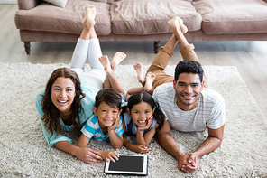 Portrait of parents and children lying on rug and using digital tablet at home