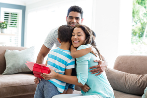 Mother receiving a gift from his kids and husband in living room at home