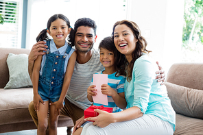 Portrait of parents and kids sitting on sofa with present in living room at home