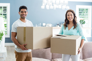 Portrait of couple holding card boxes in living room at home