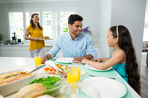 Daughter and parents interacting while having meal on table at home