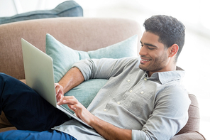 Man sitting on sofa and using laptop in living room at home