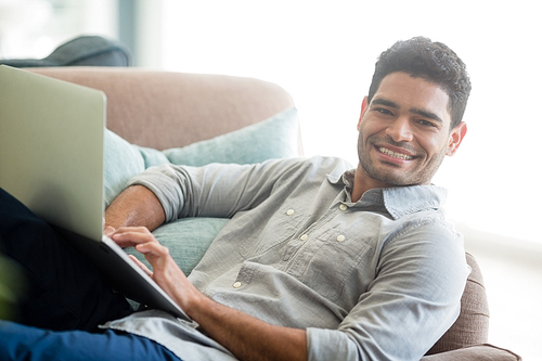 Portrait of man sitting on sofa and using laptop in living room at home