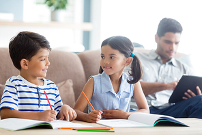 Smiling siblings doing homework in living room at home