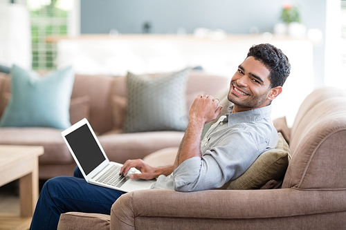 Portrait of man sitting on sofa and using laptop in living room at home