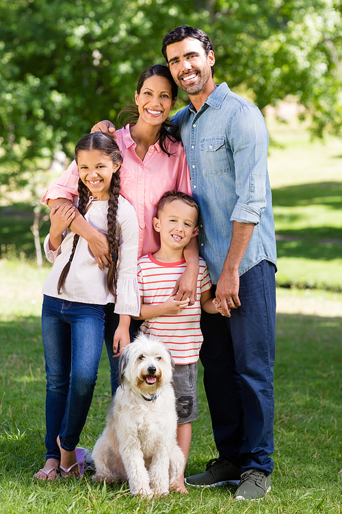 Portrait of happy family with their pet dog standing in park on a sunny day