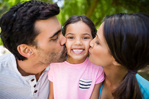 Smiling girl being kissed by his parents in park