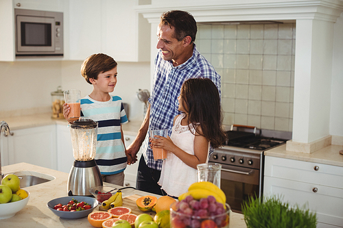 Father and kids holding glass of smoothie in kitchen
