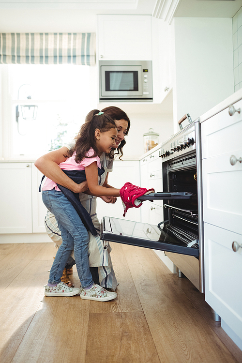 Mother and daughter placing tray of cookies in oven at kitchen
