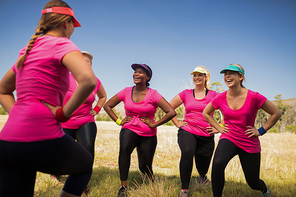 Female trainer assisting woman while exercising in the boot camp on a sunny day