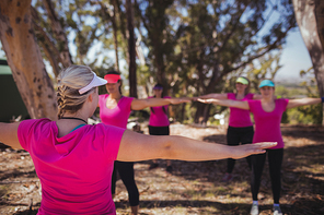 Female trainer instructing women while exercising in the boot camp on a sunny day