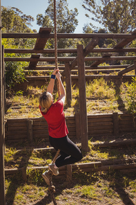 Fit woman climbing a rope during obstacle course in the boot camp