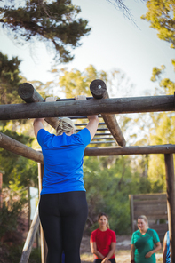 Rear view of woman climbing monkey bars during obstacle course training in the boot camp