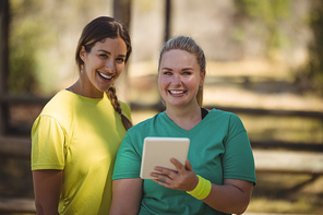 Portrait of happy friends holding digital tablet during obstacle course in boot camp