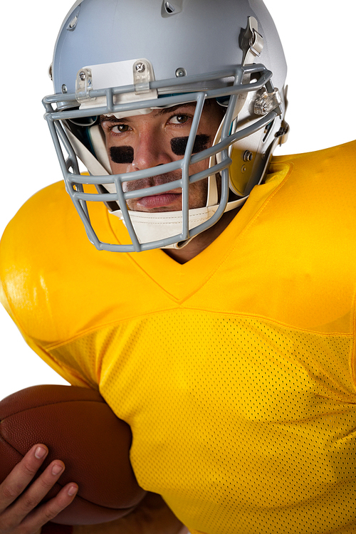 Portrait of determined football player wearing helmet holding ball while standing against white background