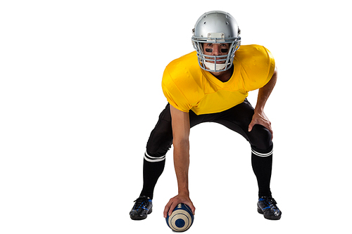 Portrait of American football player wearing helmet bending while holding ball against white background