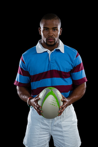 Portrait of male player holding rugby ball while standing against black background