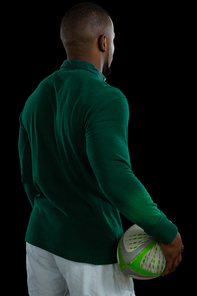 Rear view of male player holding rugby ball while standing against black background