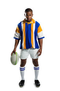 Portrait of confident rugby player holding ball while standing against white background