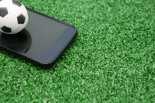 Close-up of football and mobile phone on artificial grass