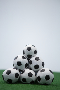 Stack of piled up football soccer balls on artificial grass against white background