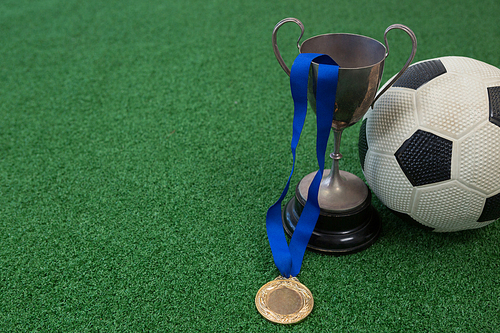 Close-up of football, trophy and medal on artificial grass