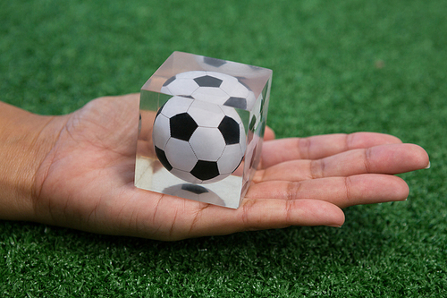 Close-up of hand holding acrylic football cube on artificial grass