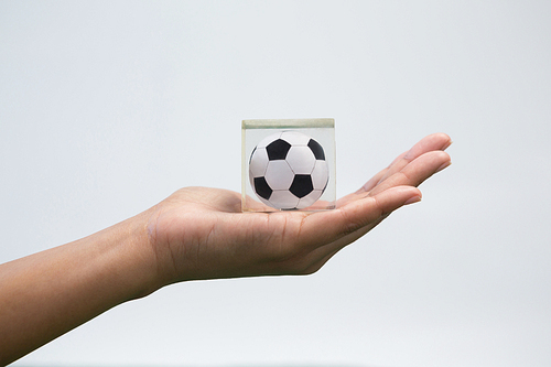 Close-up of hand holding acrylic football cube against white background