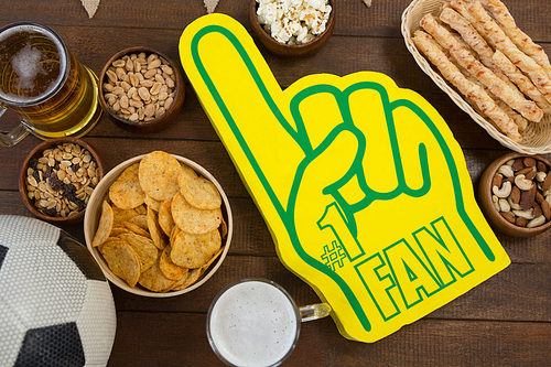 Close-up of foam hand, snacks and football on wooden table