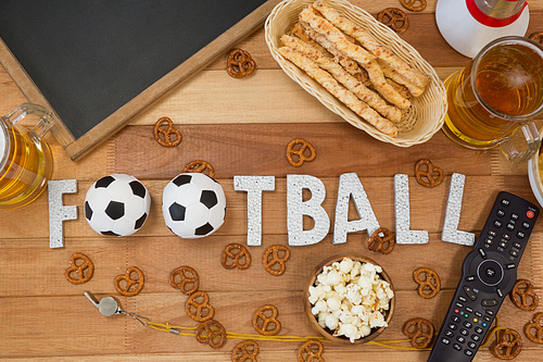 Overhead of remote control, slate, snacks, drinks and football word arranged on table