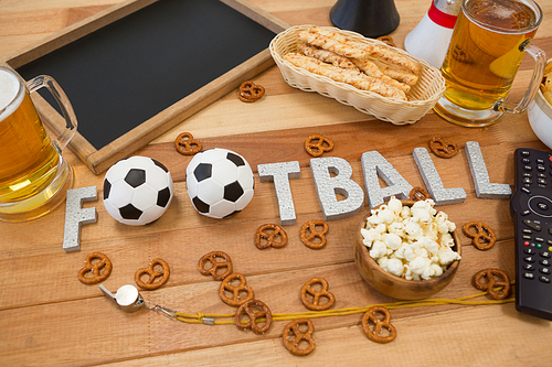 Close-up of remote control, slate, snacks, drinks and football word arranged on table