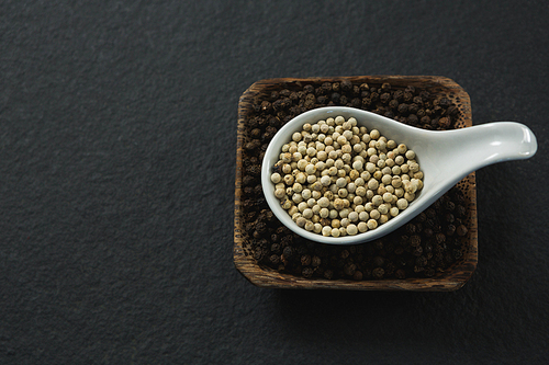 Black pepper and white pepper seeds in a bowl on black background