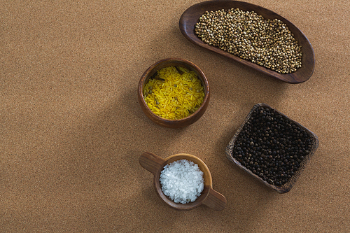 Coriander seeds, rice, black pepper seed and salt in bowl on brown background