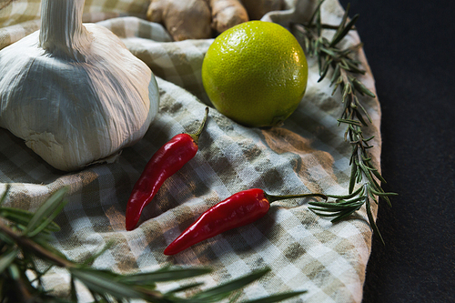 Close-up of garlic, red chili pepper, sweet lime and rosemary on table cloth