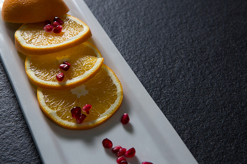Slice of orange with pomegranate seeds in tray on black background
