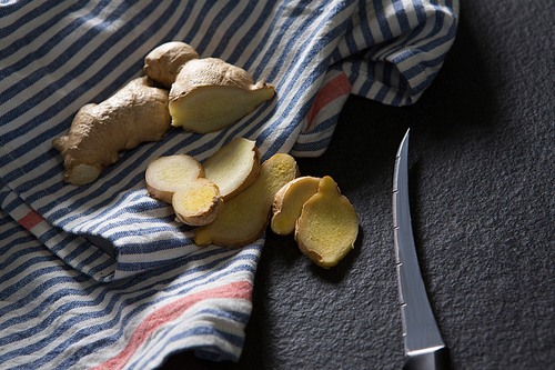 Close-up of sliced ginger with knife and napkin on black background