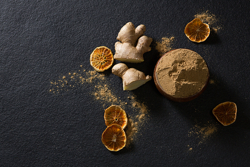 Bowl of ginger powder with ginger and dried lemon on black background