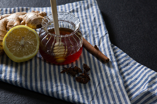 Overhead of ginger, star anise, cinnamon, lemon and honey in jar on textile