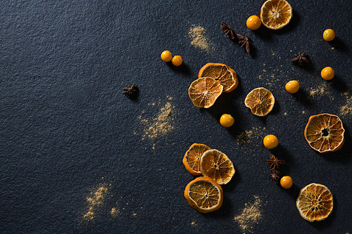 Overhead of dried orange with star anise and golden berries on black background