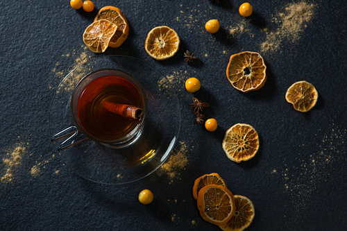Cup of tea with cinnamon stick and fruits on black background