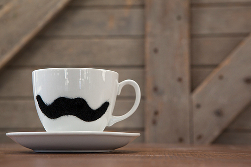 Close up of white coffee cup with black mustache on wooden table