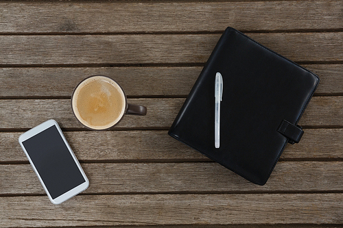 Overhead of mobile phone, coffee, pen and organizer on wooden plank