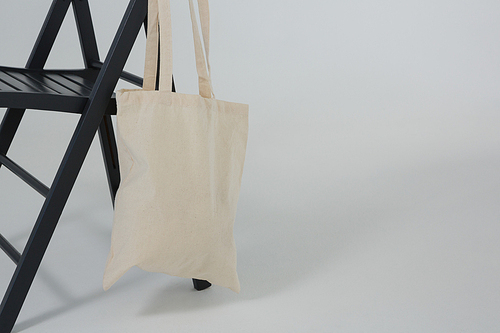 Beige bag hanging on a black chair on grey background