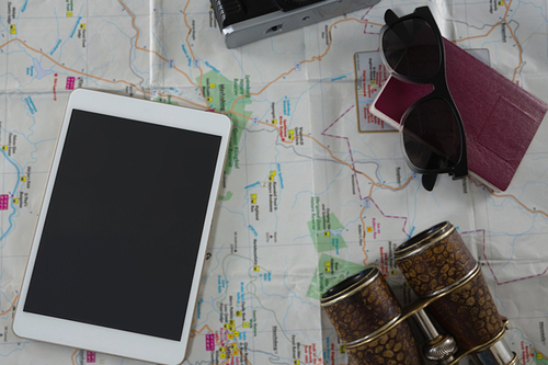 Overhead of passport, camera, binoculars and digital tablet on map